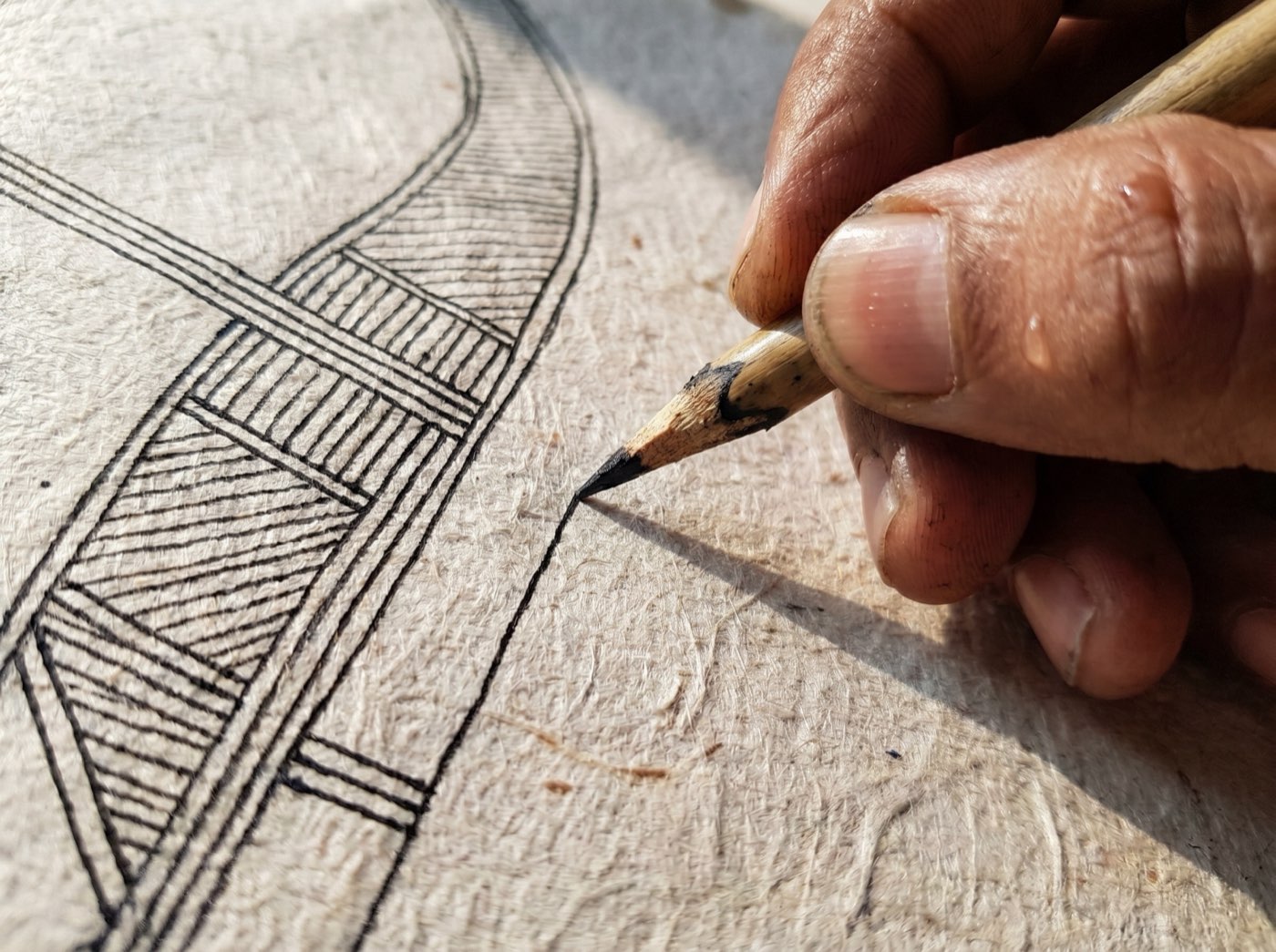 Close study of a heritage artisan's hand rendering fine Madhubani linework in ink on cold-pressed paper.