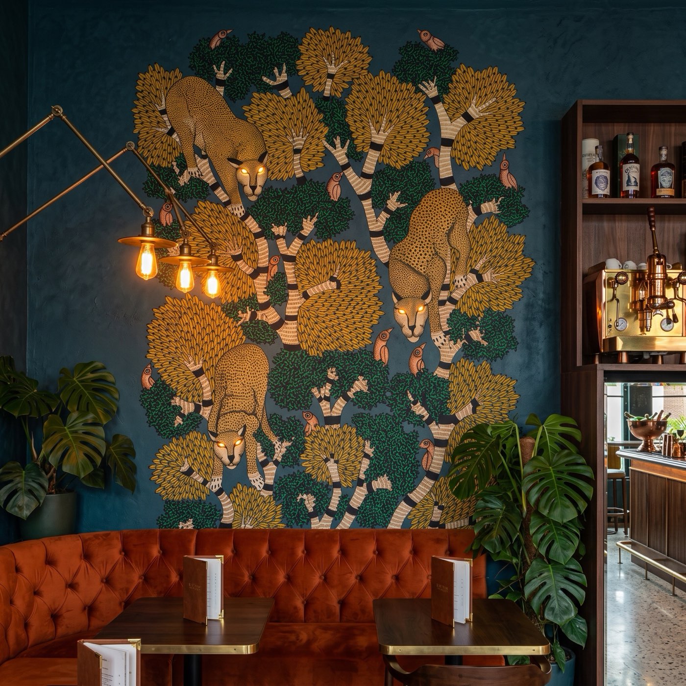 Jewel-toned Gond feature wall of three leopards prowling a bird-filled tree canopy in a boutique cocktail lounge.
